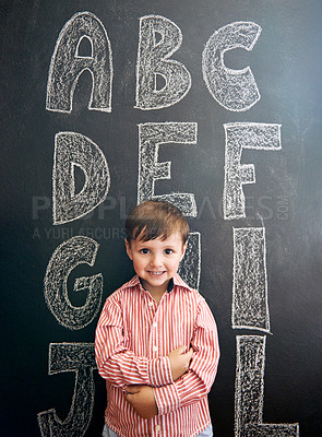 Buy stock photo Portrait of an adorable little boy standing in front of a blackboard with letters written on it