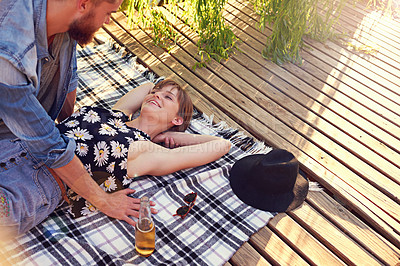 Buy stock photo Couple, love and relax on blanket in nature with bonding, connection and anniversary date with smile. People, alcohol and holiday fun at pier outdoor for commitment, relationship or loyalty with care