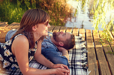 Buy stock photo Shot of an affectionate young couple lying on a blanket outdoors