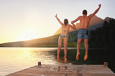 Buy stock photo Rearview shot of a young couple in swimsuits leaping of a dock at sunset