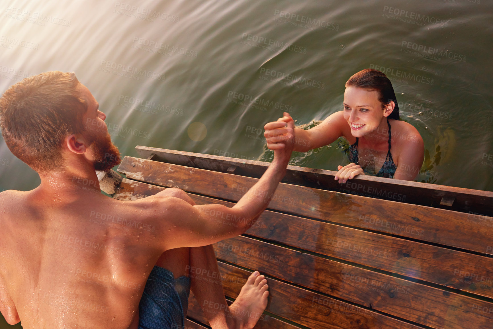 Buy stock photo Shot of a young man helping his girlfriend out of the water