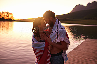 Buy stock photo Shot of an affectionate young couple in swimsuits wrapped in a towel at a lake