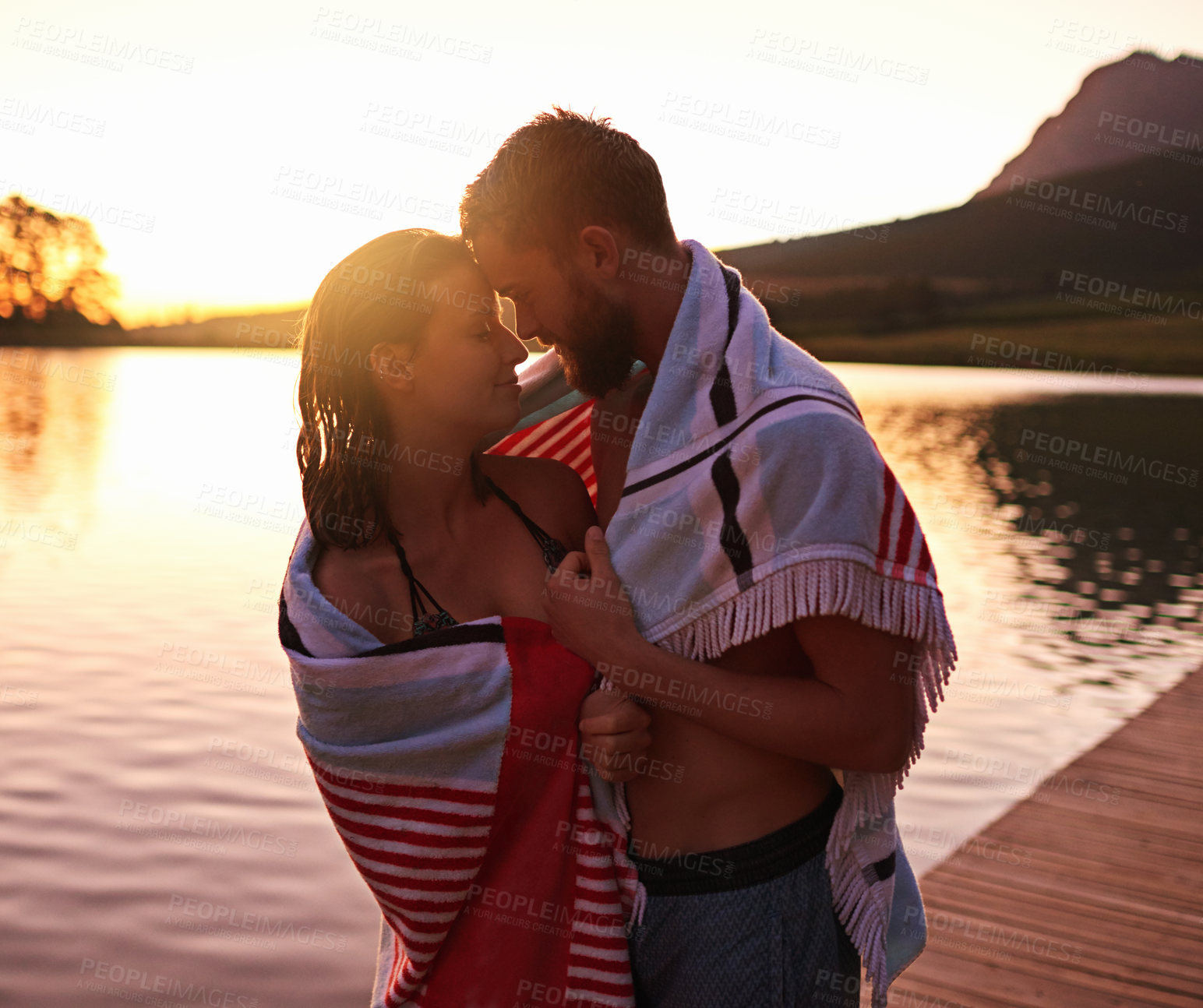 Buy stock photo Love, sunset or couple with towel at lake together on vacation, anniversary and outdoor holiday. Relationship, relax or people hug on dock for bonding, swimming and care on romantic honeymoon date