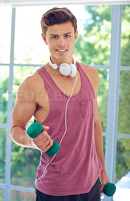 Buy stock photo Shot of a young man holding dumbbells and wearing a set of headphones around his neck