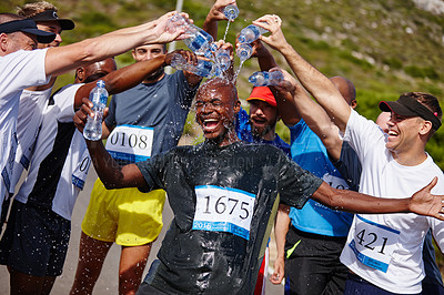 Buy stock photo Shot of a group of young men pouring water over their friend after running a marathon