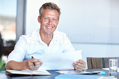 Buy stock photo Shot of a handsome businessman going through his paperwork in the office