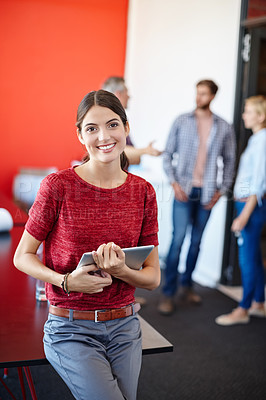 Buy stock photo Shot of a young designer using a tablet with her colleagues standing in the background