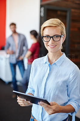 Buy stock photo Shot of a young designer using a tablet with her colleagues standing in the background