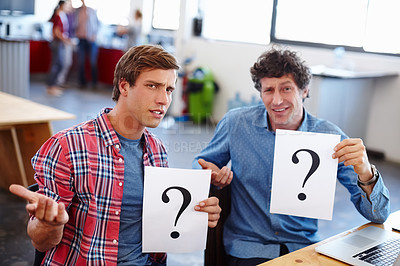 Buy stock photo Portrait of two coworkers looking confused while holding question mark signs