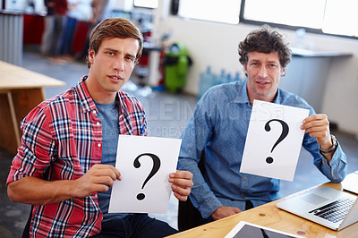 Buy stock photo Portrait of two coworkers looking confused while holding question mark signs