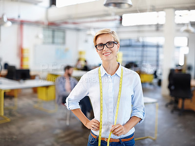 Buy stock photo Portrait of a young woman standing with a tape measure around her neck and colleagues colleagues in the background