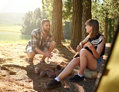 Buy stock photo Shot of a young woman playing guitar for her boyfriend at their campsite