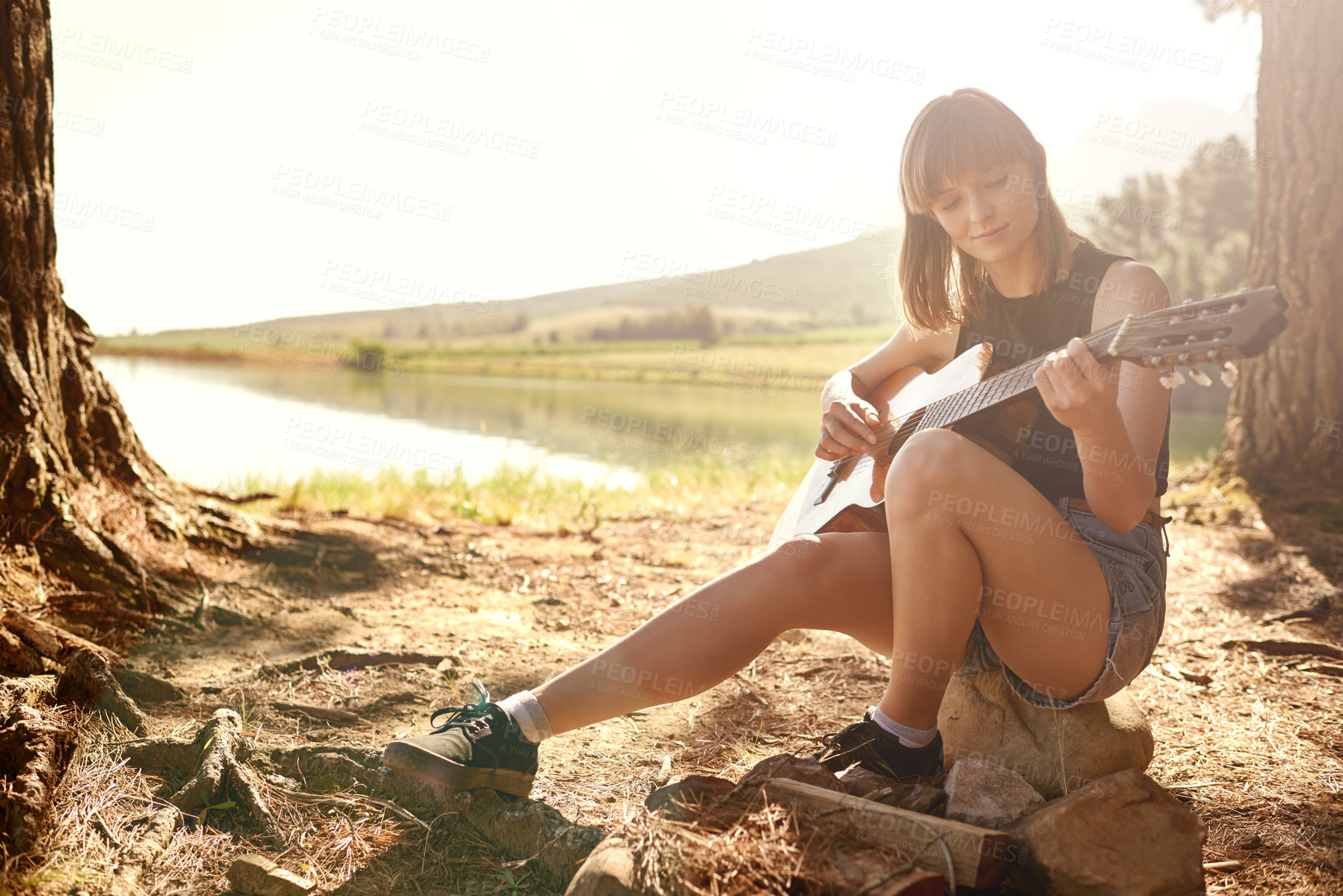 Buy stock photo A young woman playing guitar while camping