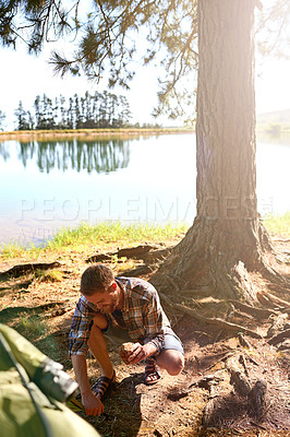 Buy stock photo Shot of a young man setting up a tent while on a camping trip