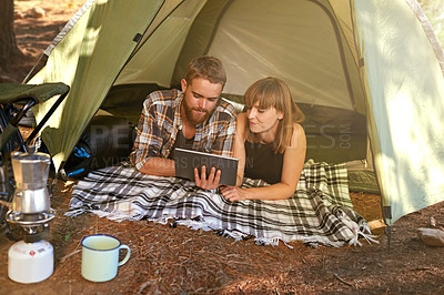 Buy stock photo Shot of a young couple lying in a tent looking using a digital tablet