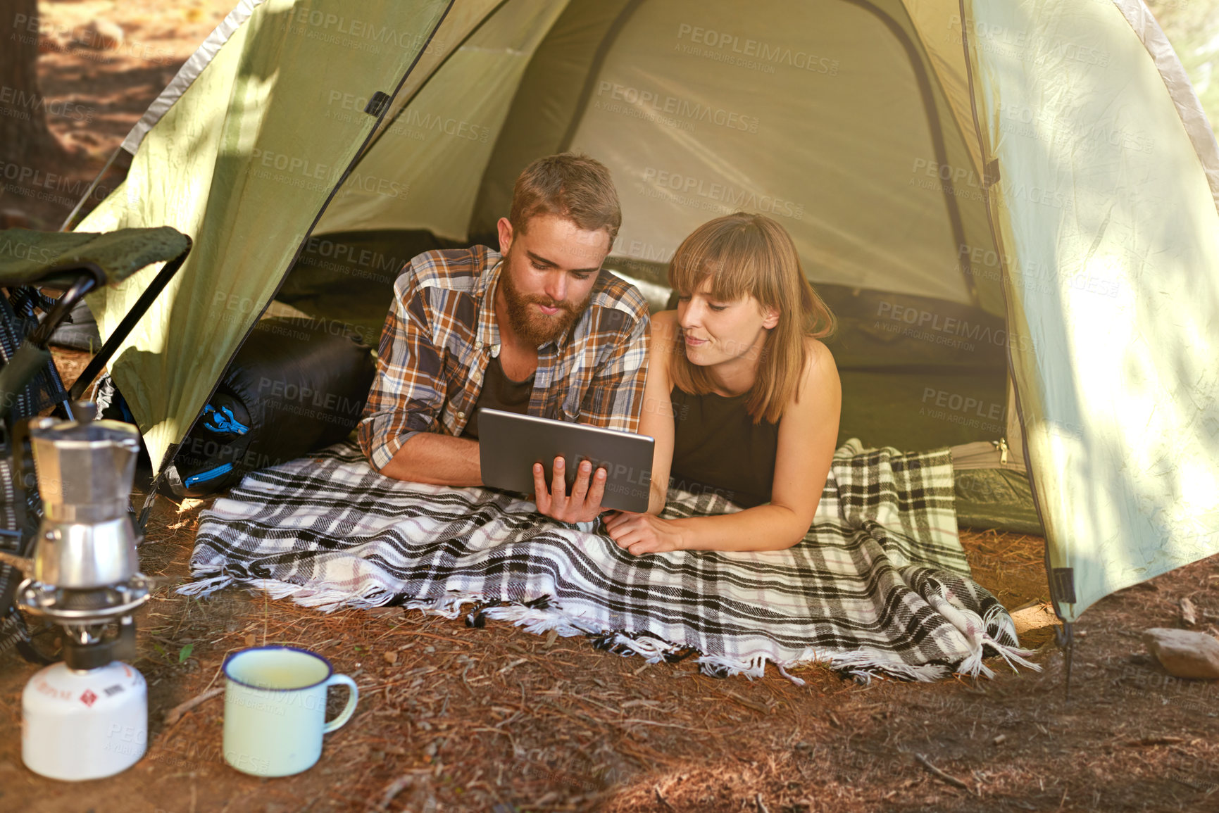 Buy stock photo Shot of a young couple lying in a tent looking using a digital tablet