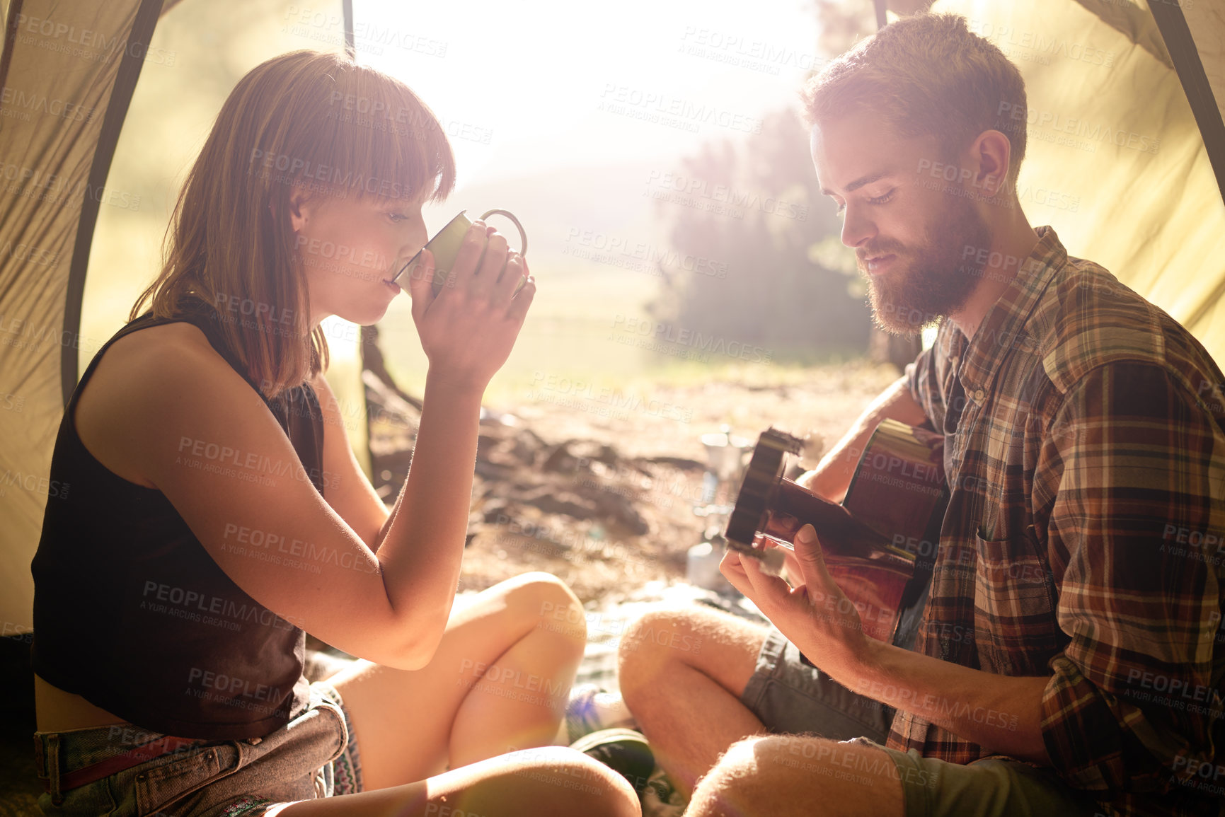 Buy stock photo Shot of a young man playing guitar to his girlfriend in a tent