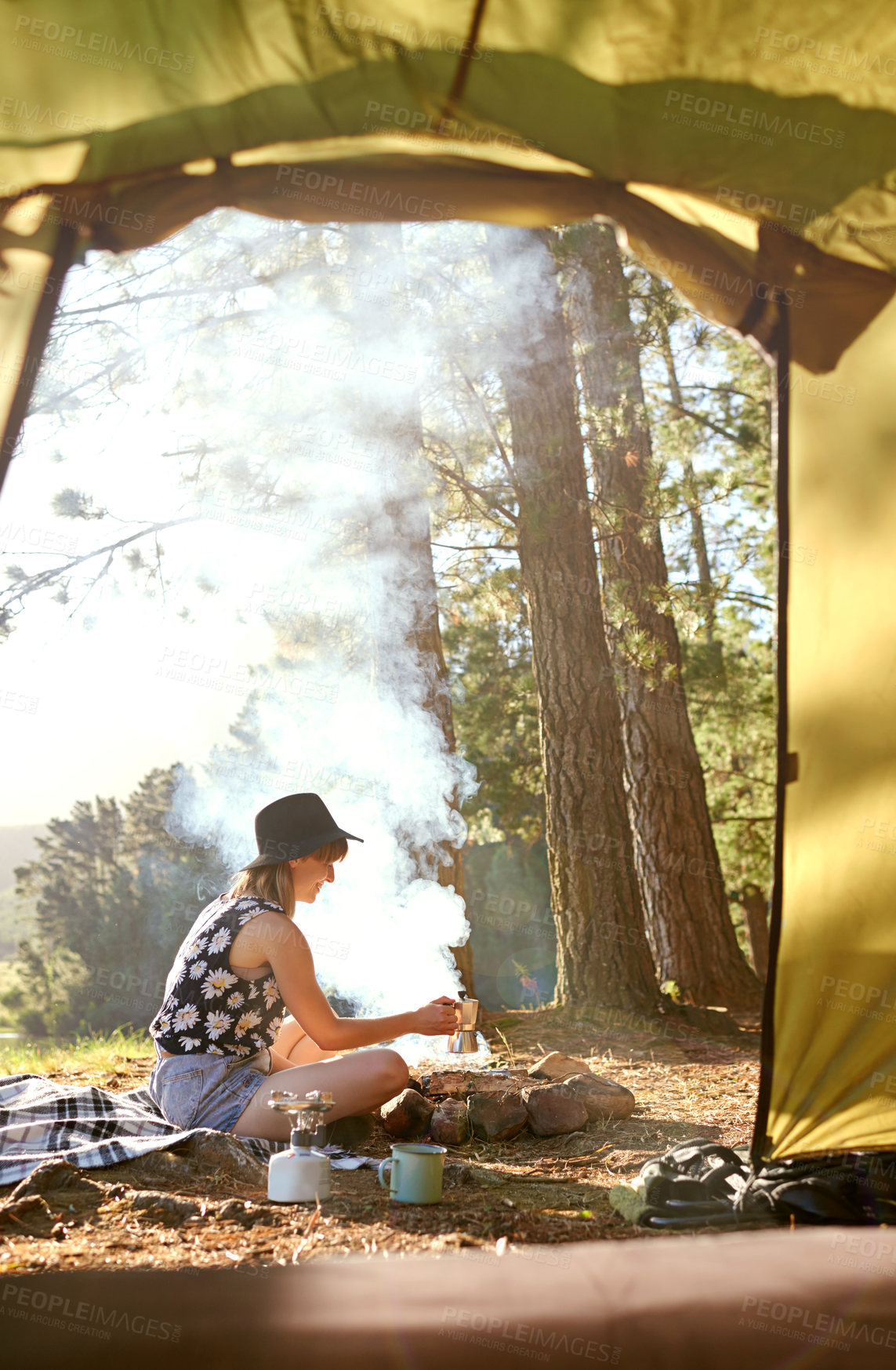 Buy stock photo Shot of a young woman making coffee over an open fire at a campsite