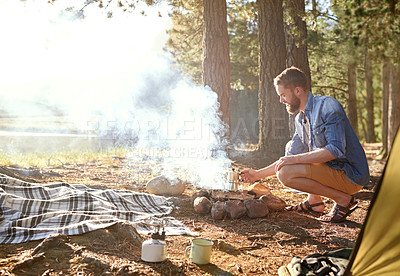 Buy stock photo Shot of a young man tending to a fire at his campsite
