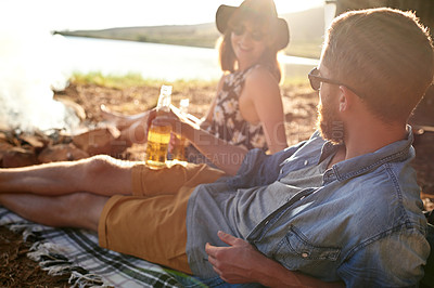 Buy stock photo Shot of a young couple drinking a beer while enjoying a day at the lake