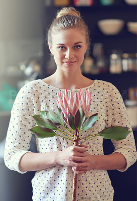 Buy stock photo Portrait of a beautiful young woman standing in her kitchen holding a protea flower