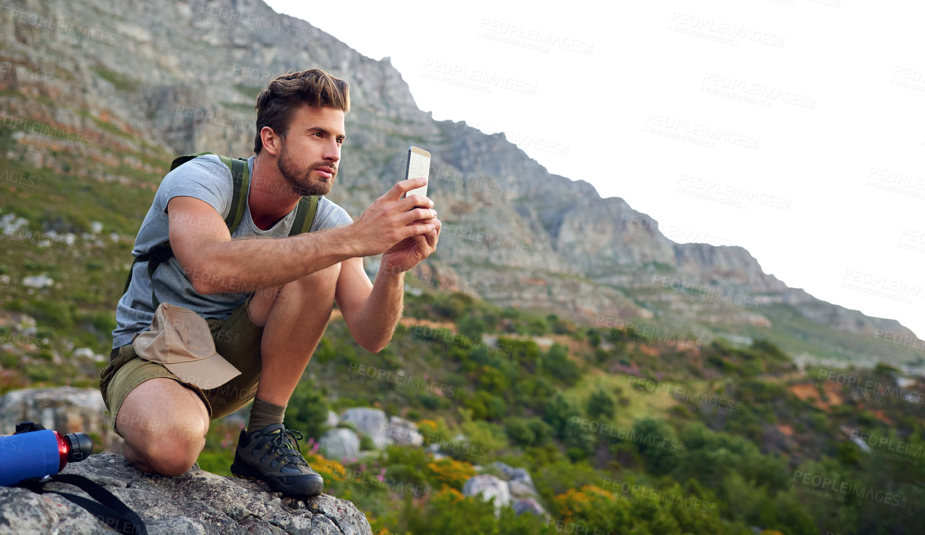 Buy stock photo Shot of a handsome young man snapping pics while hiking