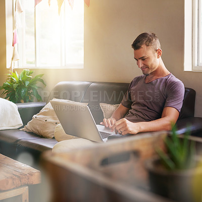 Buy stock photo Shot of a handsome young man using a laptop on the sofa at home
