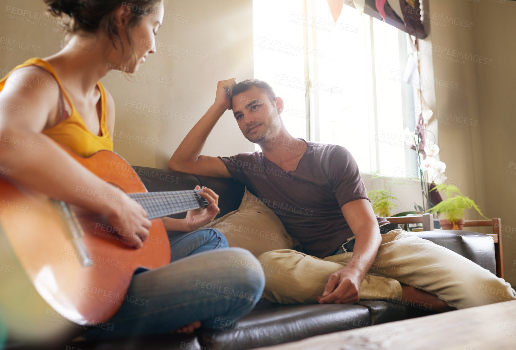 Buy stock photo Shot of a young woman playing the guitar while relaxing on the sofa with her husband