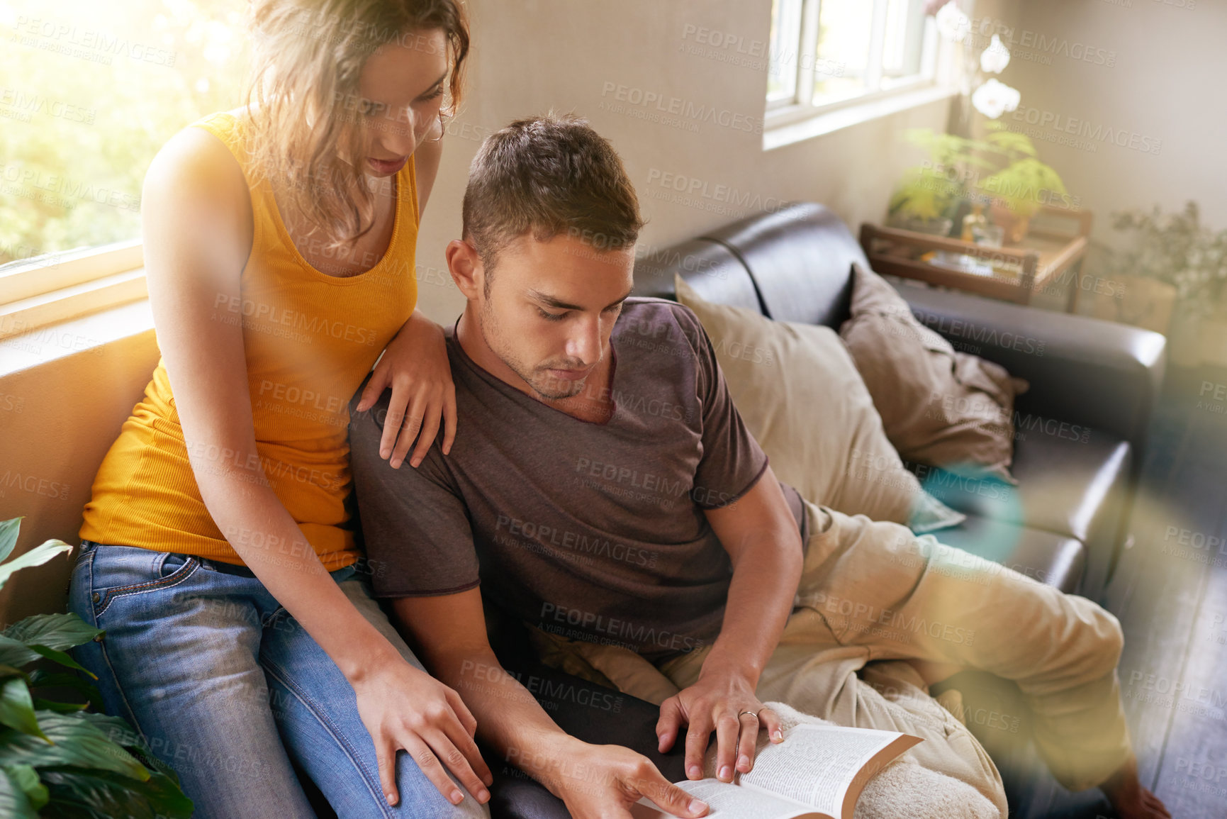 Buy stock photo Shot of a happy young  couple reading a book together while relaxing on the sofa
