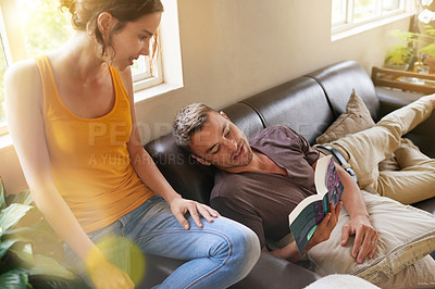 Buy stock photo Shot of a young man reading a book while relaxing on the sofa with his wife