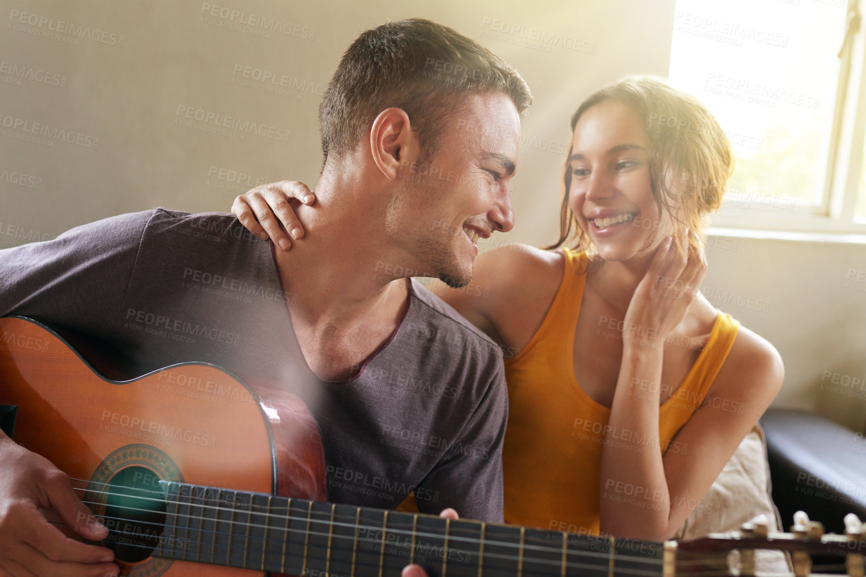 Buy stock photo Shot of a young man playing the guitar while relaxing on the sofa with his wife