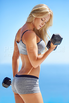 Buy stock photo Shot of a beautiful young woman lifting weights outside
