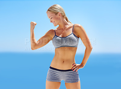 Buy stock photo Shot of an attractive young woman in exercise clothing flexing her bicep outside