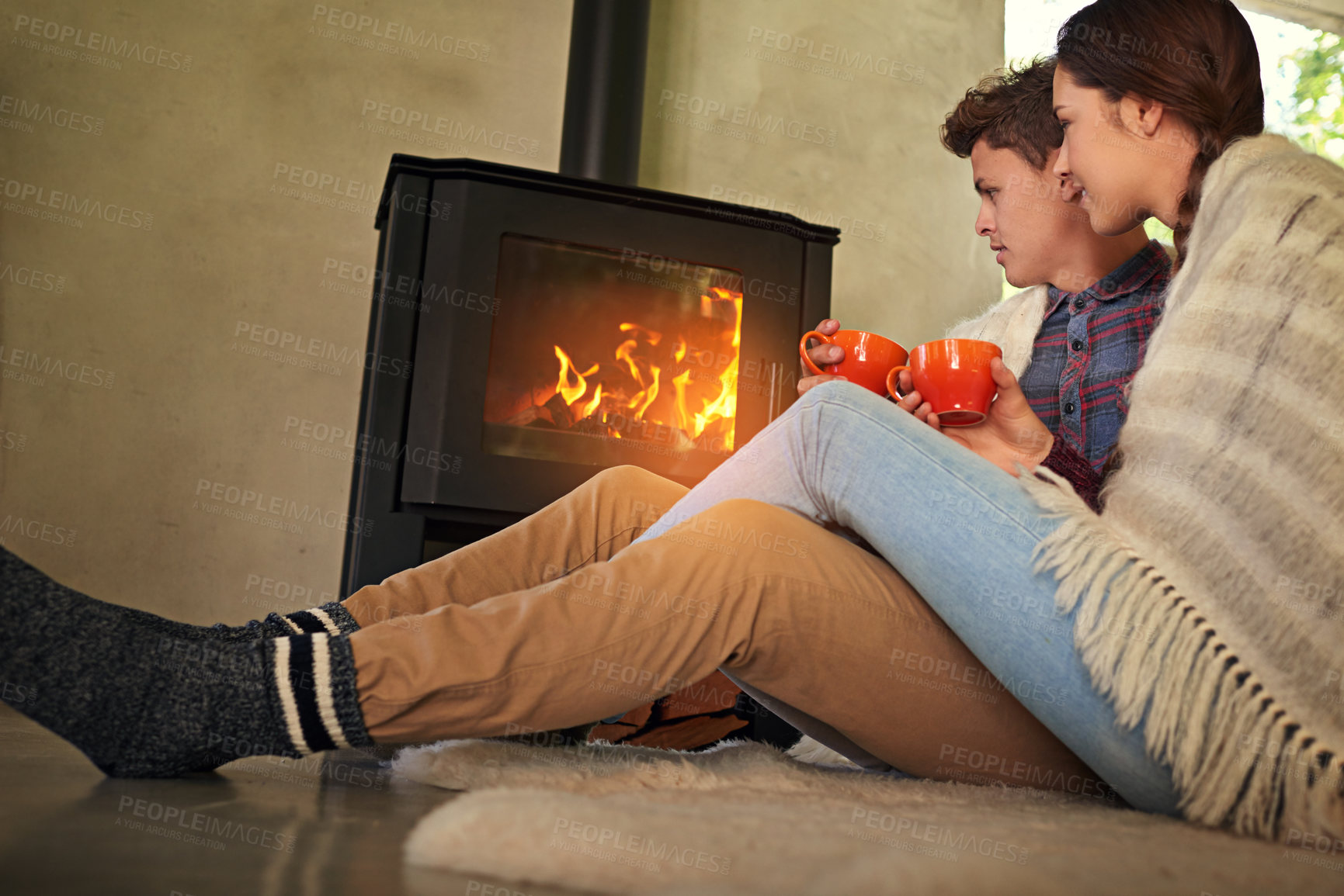 Buy stock photo Shot of a young couple drinking hot chocolate by the fireplace