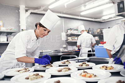 Buy stock photo Shot of a chef plating food for a meal service in a professional kitchen