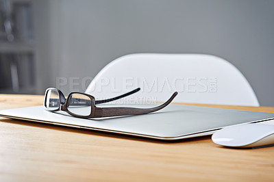 Buy stock photo Shot of a laptop and glasses on a table