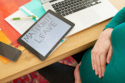Buy stock photo A pregnant woman sitting with a tablet with the words 'maternity leave' on the screen