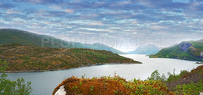 Buy stock photo Landscape of a river between hills and mountains. Green foliage by the riverbank with a blue sky in Norway. Calm water near a vibrant wilderness against a bright cloudy horizon. Peaceful nature scene