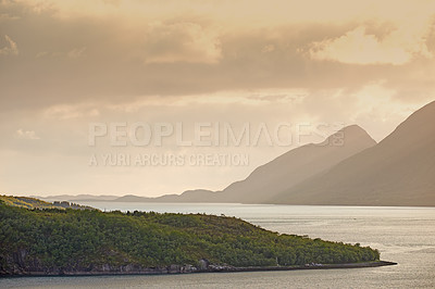 Buy stock photo Green hills by the seaside with a sunset sky in Norway. Wild vibrant landscape in Nordland. Calm sea near an uninhabited island wilderness against a warm dark cloudy horizon. A peaceful nature scene