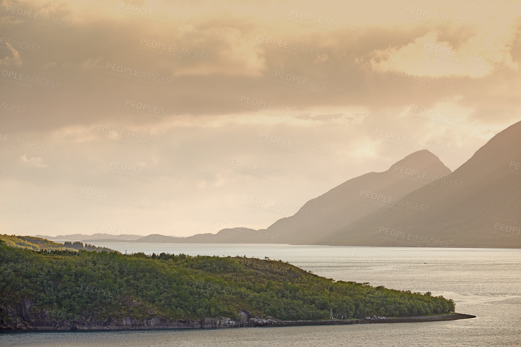 Buy stock photo Green hills by the seaside with a sunset sky in Norway. Wild vibrant landscape in Nordland. Calm sea near an uninhabited island wilderness against a warm dark cloudy horizon. A peaceful nature scene