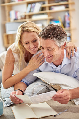 Buy stock photo Shot of a smiling mature couple lying on their living room floor looking at photographs