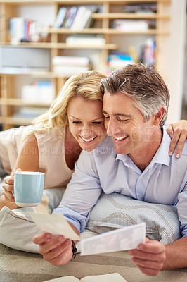 Buy stock photo Shot of a smiling mature couple lying on their living room floor looking at photographs