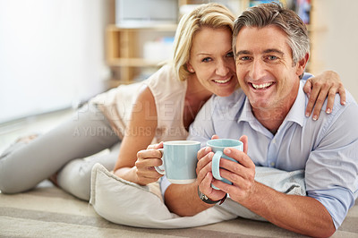 Buy stock photo Portrait of a smiling mature couple lying on their living room floor drinking coffee