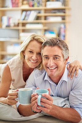 Buy stock photo Portrait of a smiling mature couple lying on their living room floor drinking coffee