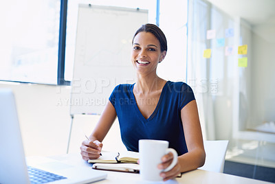 Buy stock photo A young businesswoman writing in a notebook while sitting with her laptop and cellphone