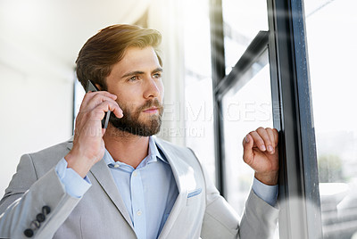 Buy stock photo Shot of a young businessman talking on his cellphone while standing by his office window