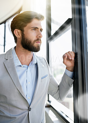 Buy stock photo Shot of an ambitious young businessman looking through his office window