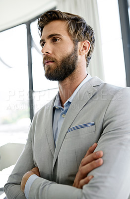 Buy stock photo Shot of an ambitious young businessman standing with his arms crossed in his office