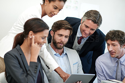 Buy stock photo Shot of a group of businesspeople looking at something on a digital tablet