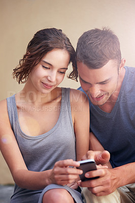 Buy stock photo Cropped shot of a young couple using a cellphone while sitting outside